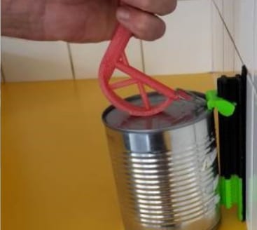 Le levier rouge imprimé en 3D, engagé dans la languette d'une boîte de conserve, actionné d'une seule main