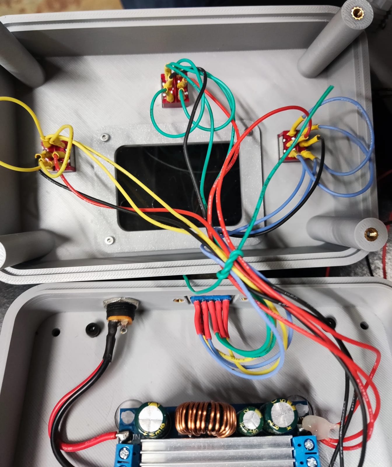 Le boîtier ouvert, vu de dessus : dans la coque du haut, les trois inverseurs rouges câblés en fils de couleur autour du cadre de la fenêtre ; dans la coque du bas, la prise jack, la prise DB9 et la carte du régulateur avec sa bobine