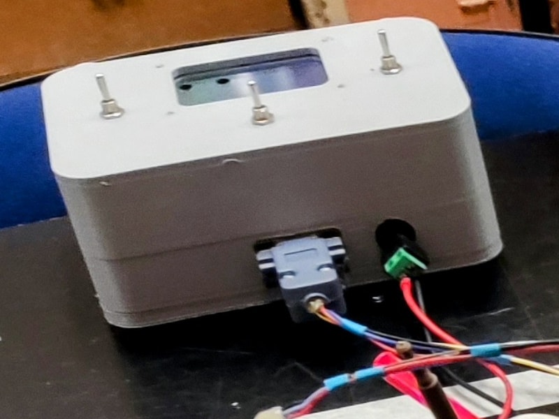 Le boîtier de commande imprimé en 3D : trois petites manettes sur le dessus autour d'une fenêtre d'acrylique, et sur le côté une prise DB9 d'où part le câble du robot, à côté de la prise d'alimentation