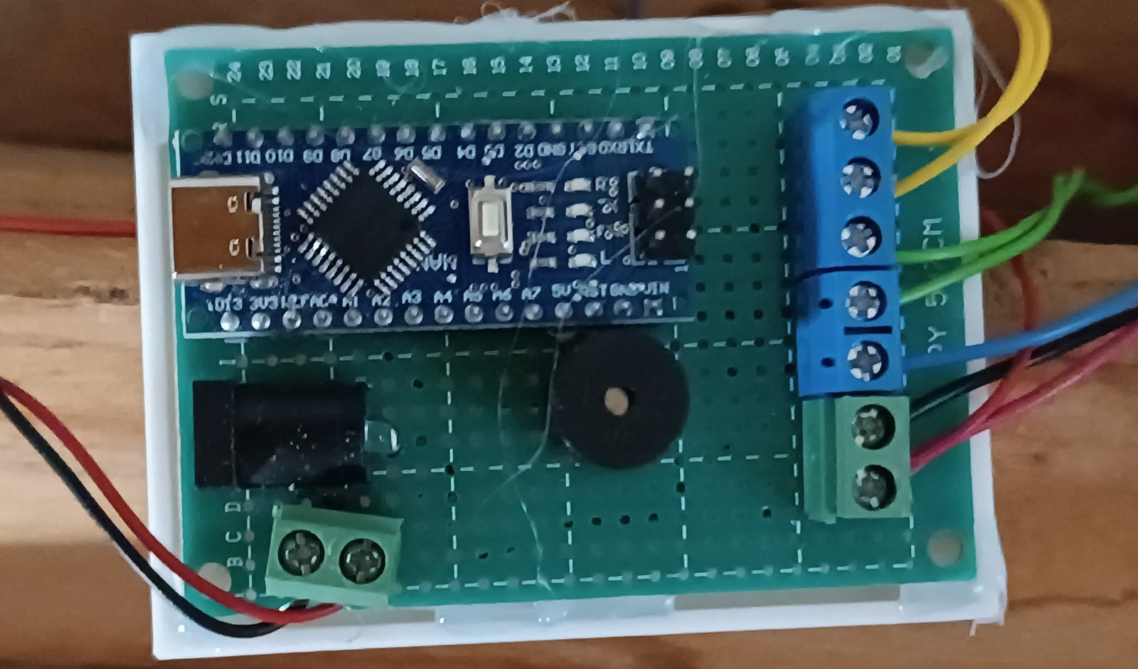 La carte électronique dans son support : l'Arduino Nano sur la plaque à pastilles, le buzzer, la prise d'alimentation et les borniers à vis d'où partent les fils des boutons et de la bande